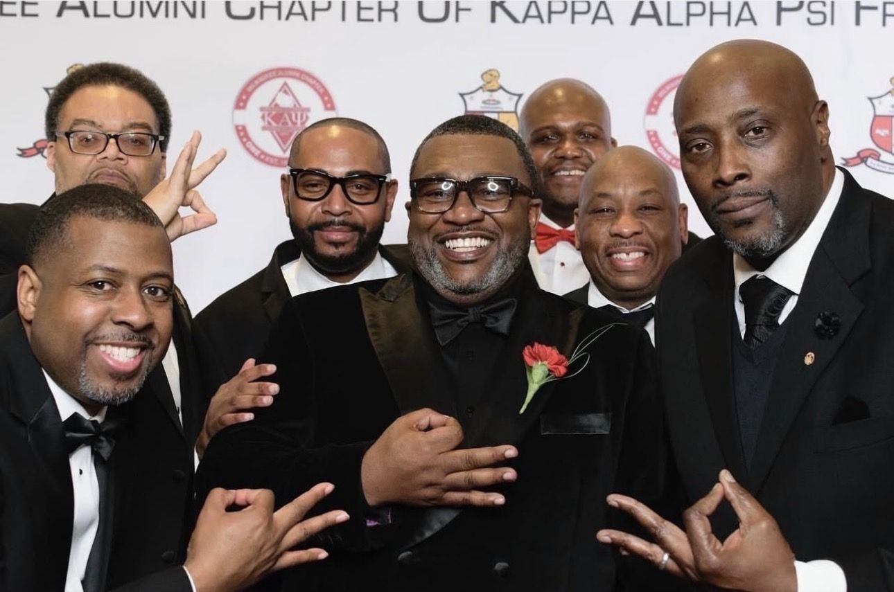 Brothers in black tie celebrating in front of the chapter banner