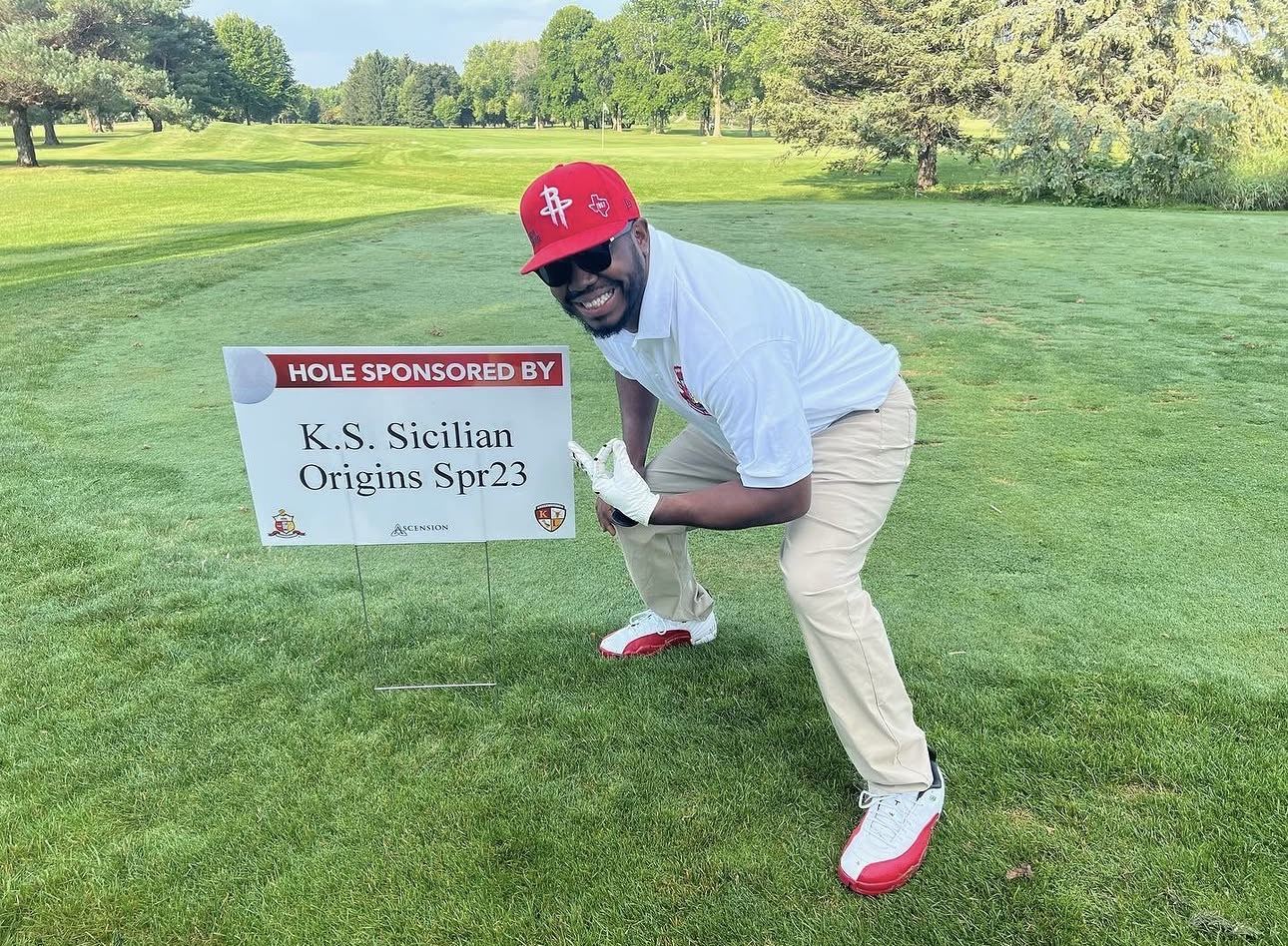 A brother on the course next to a hole sponsor sign at the Kappa League Charity Golf Outing